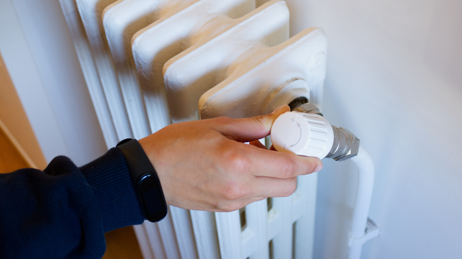 Person turning down the heat on their radiator using the dial showing a way to help manage your bills in winter.